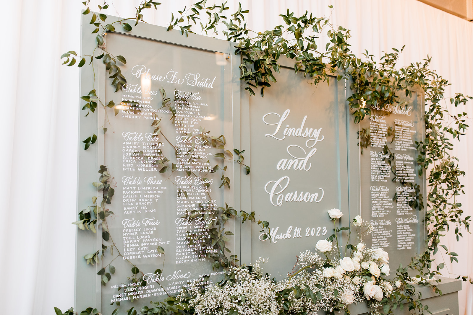 Florals cascading down a soft gray, wooden seating chart with white ink on acrylic signage