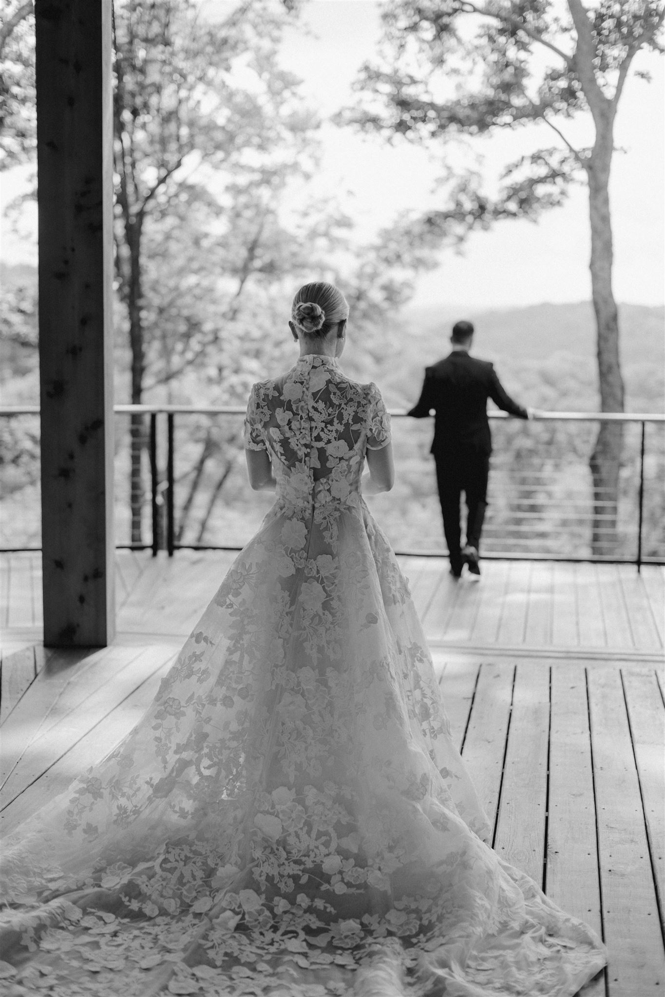 Black and white image of Bride walking towards groom who is turned away from her on outside patio deck.