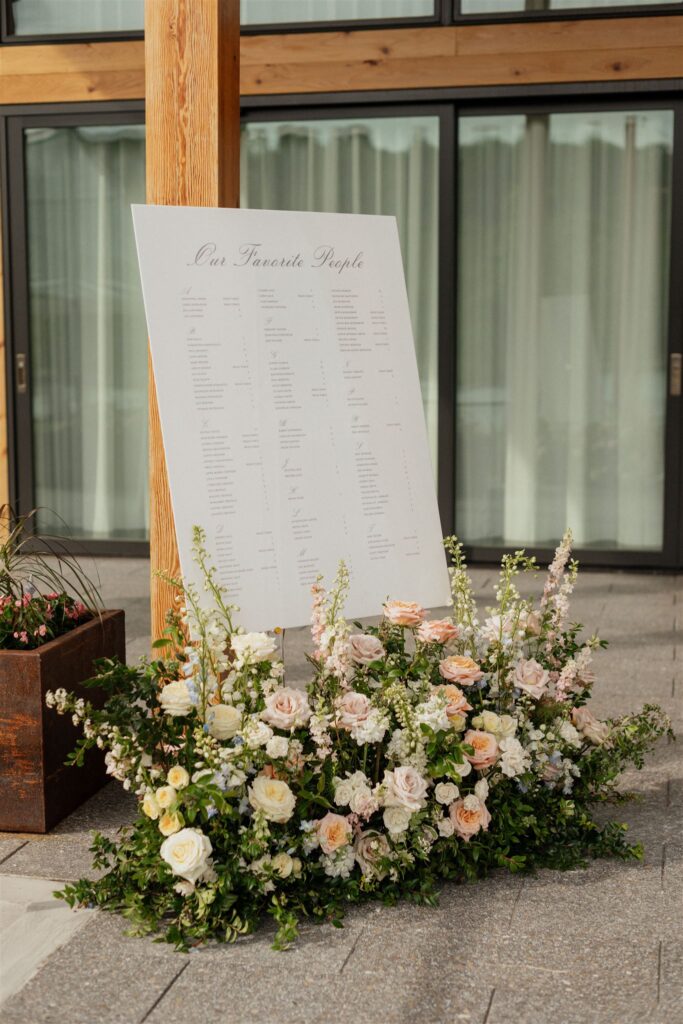 Wedding reception white, rectangle seating chart with floral arrangements placed beneath.