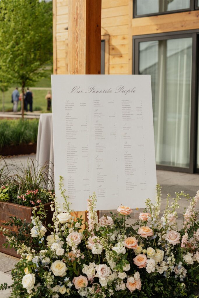 Wedding reception white, rectangle seating chart with floral arrangements placed beneath.