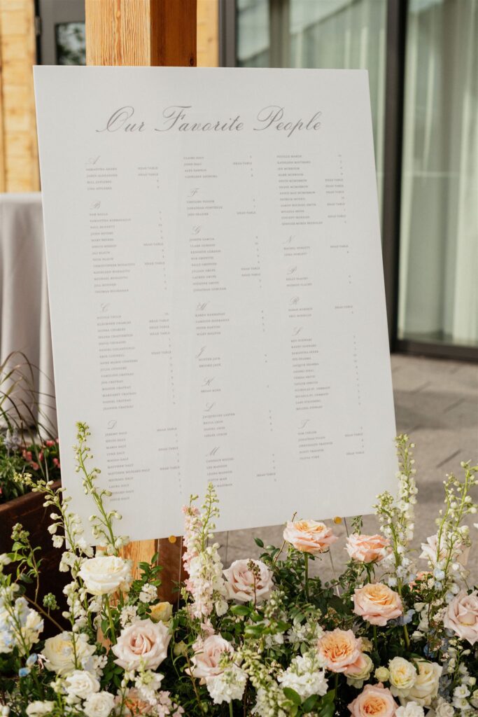 Wedding reception white, rectangle seating chart with floral arrangements placed beneath.