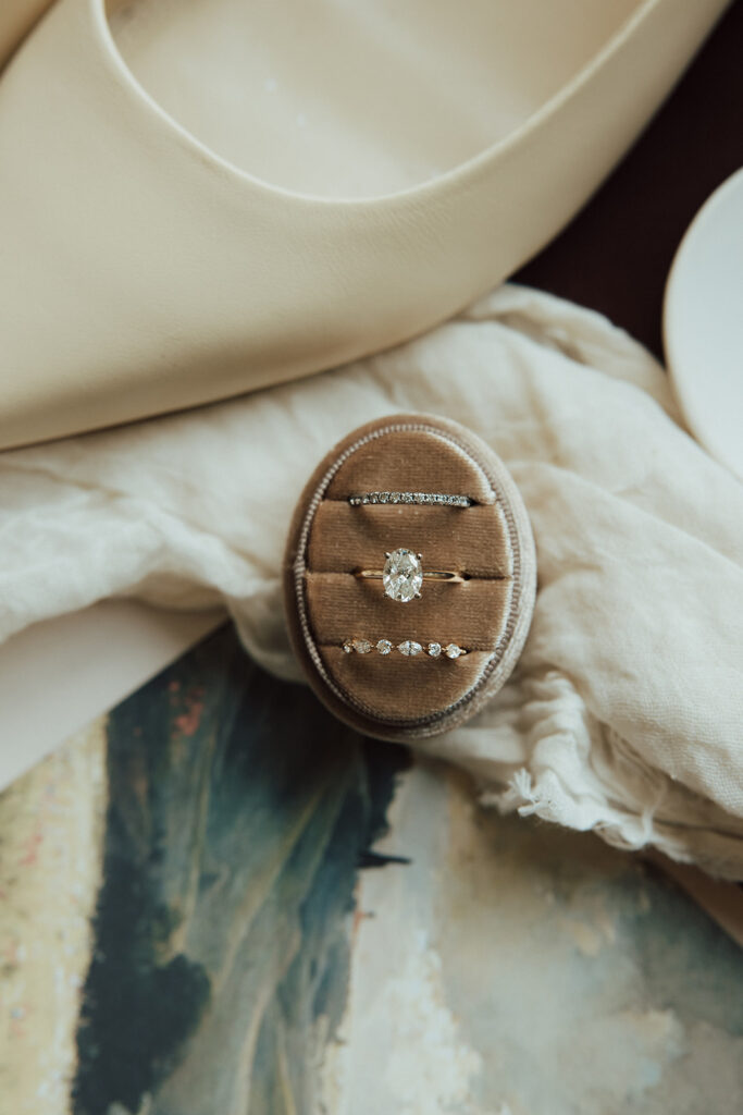 Styled flat-lay to include invitation suite, showcasing custom envelope liner of hills and countryside scene. ring box is placed in center of flat-lay.