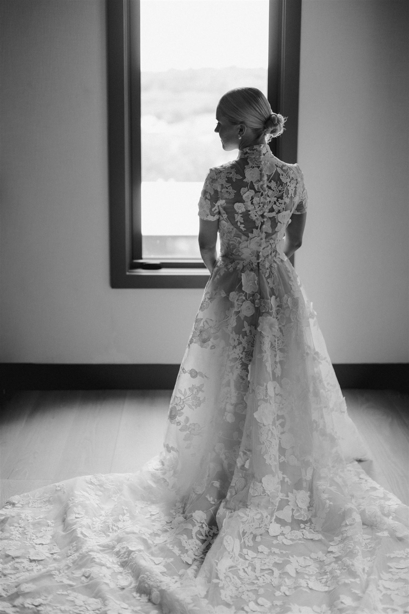 Black and white image of bride in gown with her back towards the camera looking off to the side.