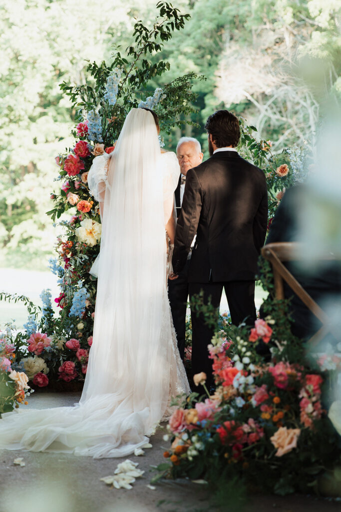 Bride and Groom stand hand in hand at ceremony, facing officiant