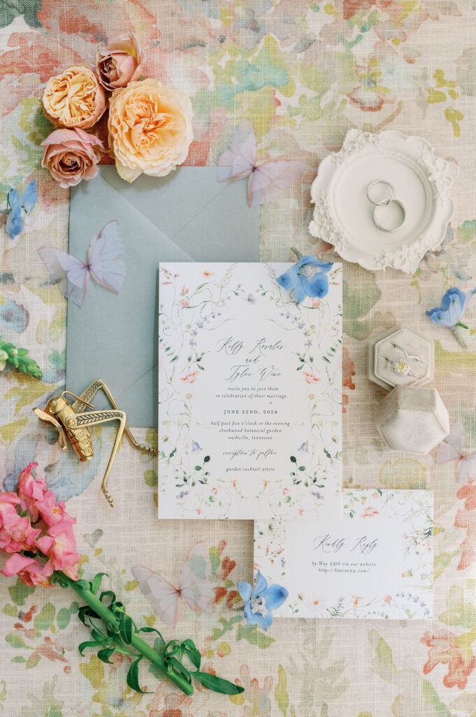 Flat lay of 2-piece wedding invitation suite styled with florals and jewelry.