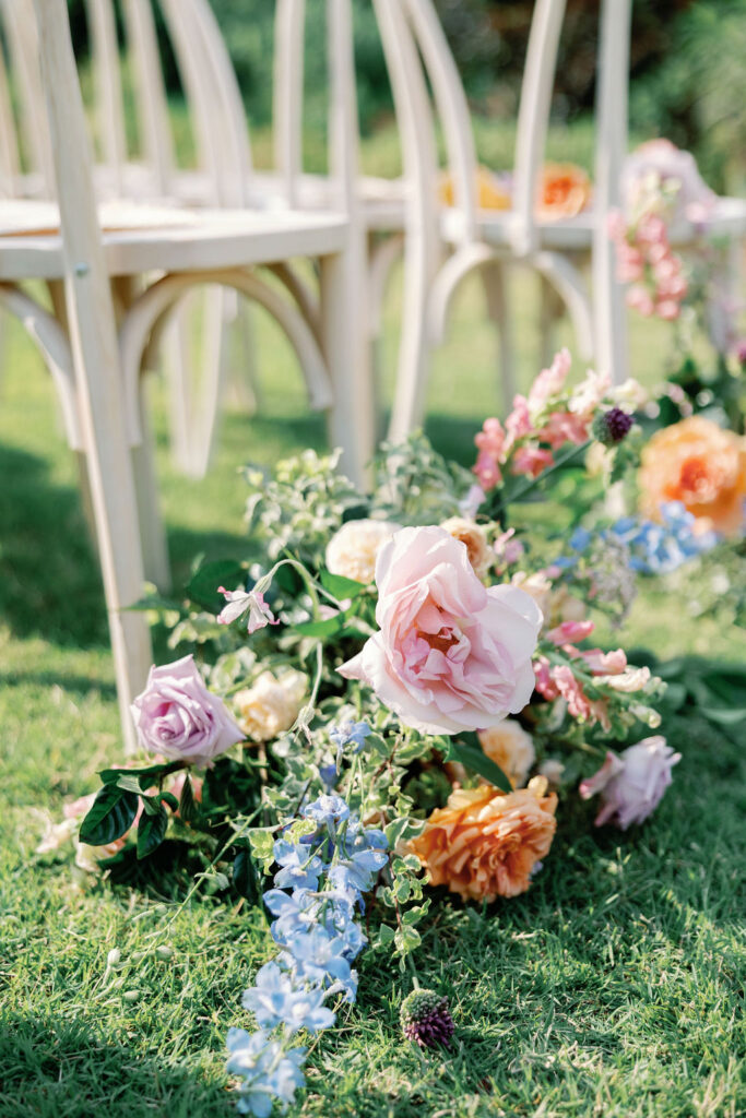 floral arrangements line the aisle of an outdoor wedding venue.