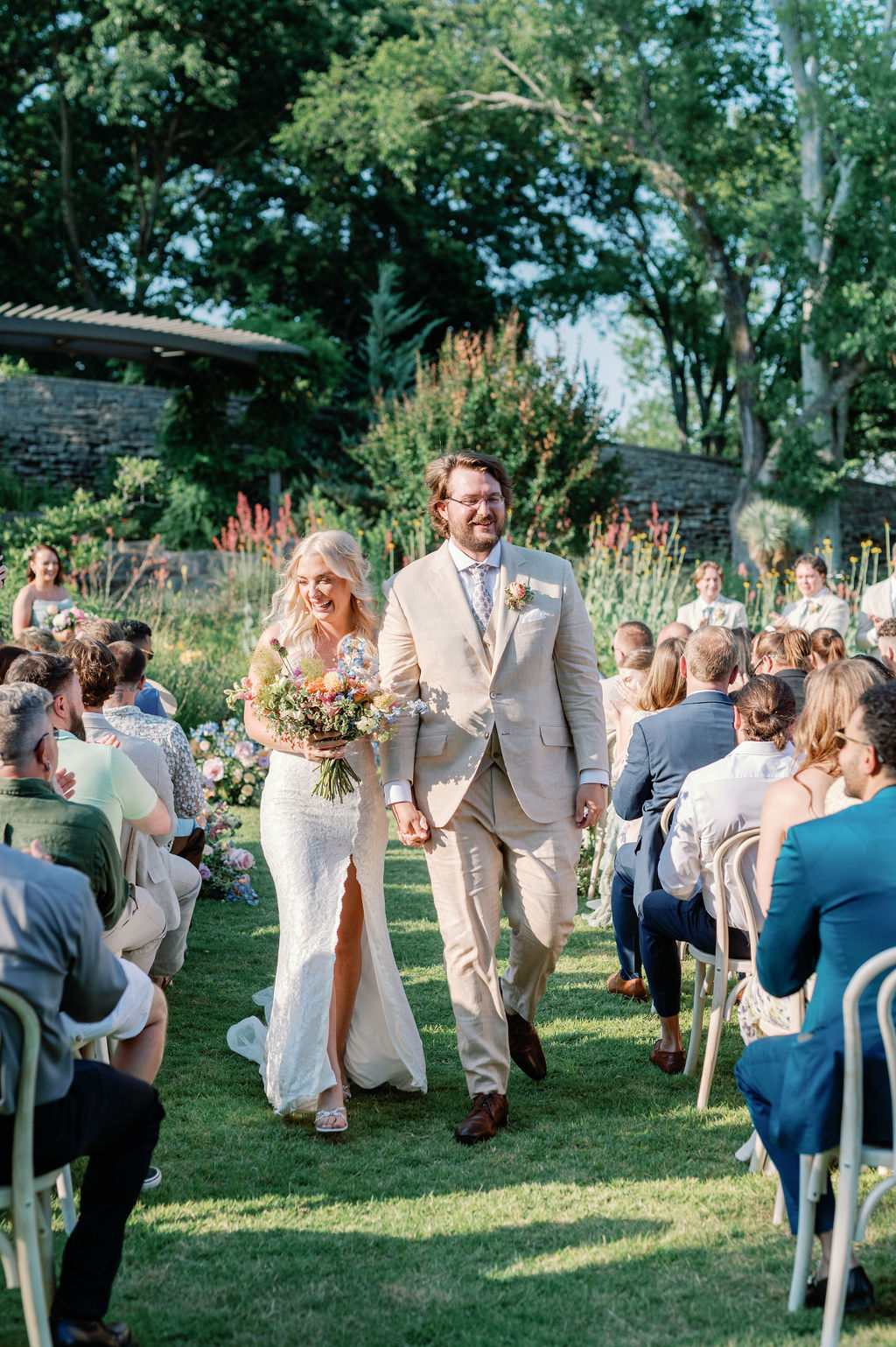 Bride and Groom walking together up the aisle after ceremony hand in hand. Bride holds bouquet of flowers.