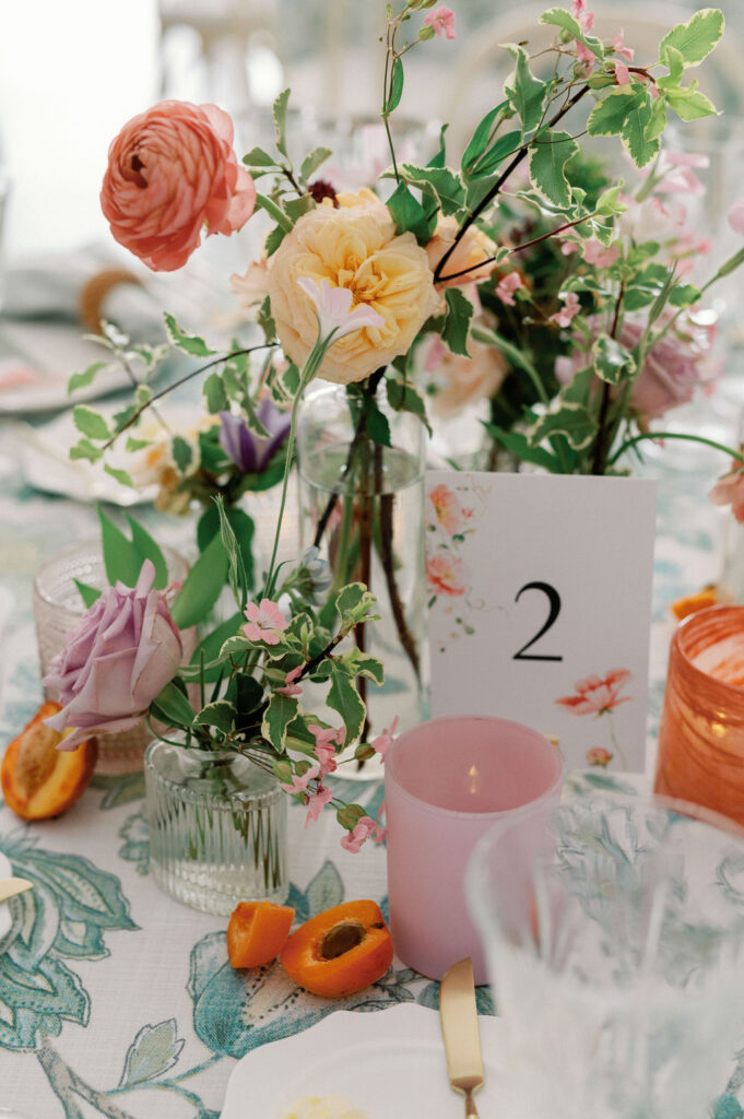 Formal wedding reception tablescape complete with florals, glassware, plates, cutlery, candles, and custom table numbers.