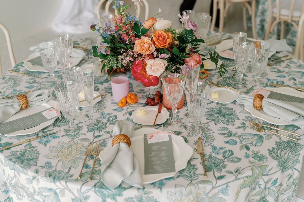 Formal wedding reception tablescape complete with florals, glassware, plates, cutlery, candles, and custom table numbers and menus.