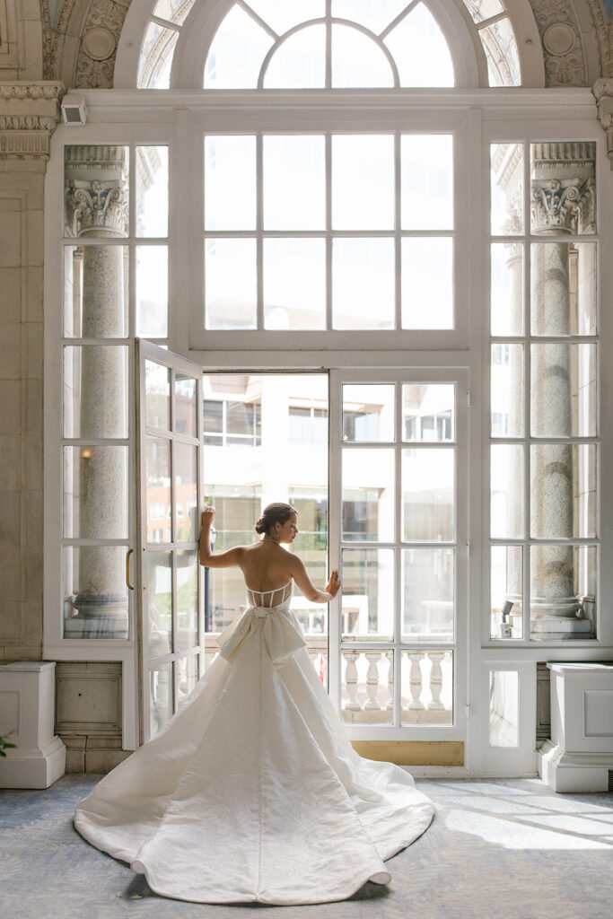 Bride faces windowed balcony in a pose.