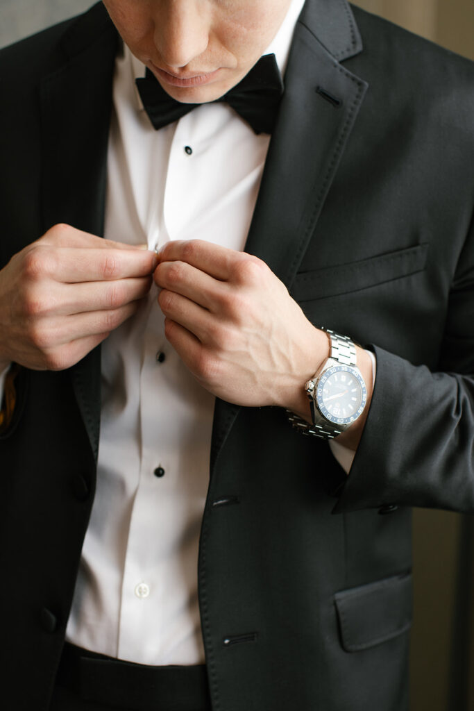 Groom adjusting a button on his tuxedo shirt.