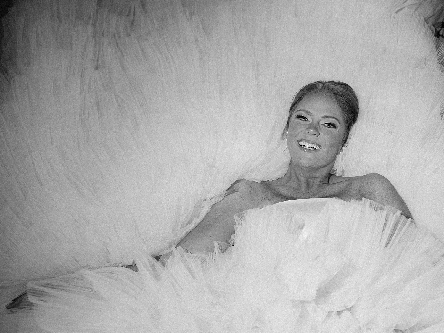 bride lays surrounded by tulle of skirt on wedding dress