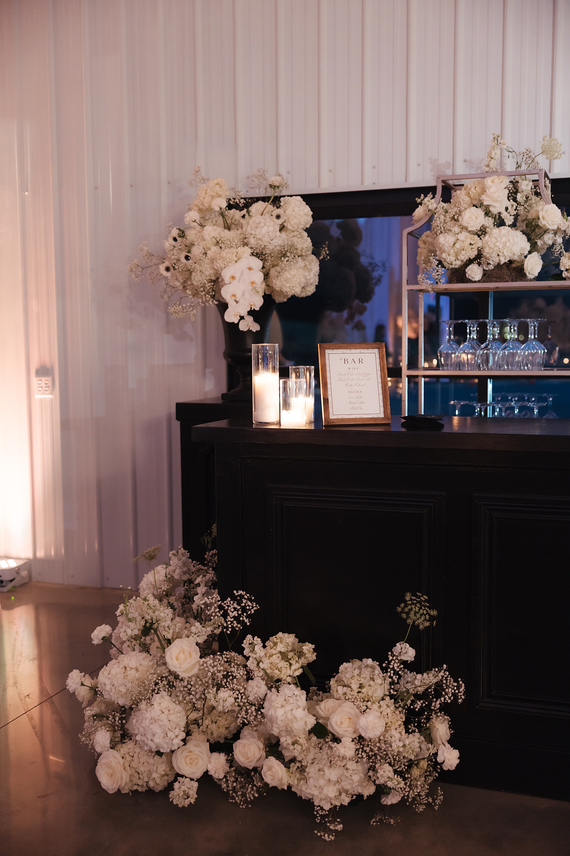 white flower bouquets sit on black bar with custom bar sign by White Ink