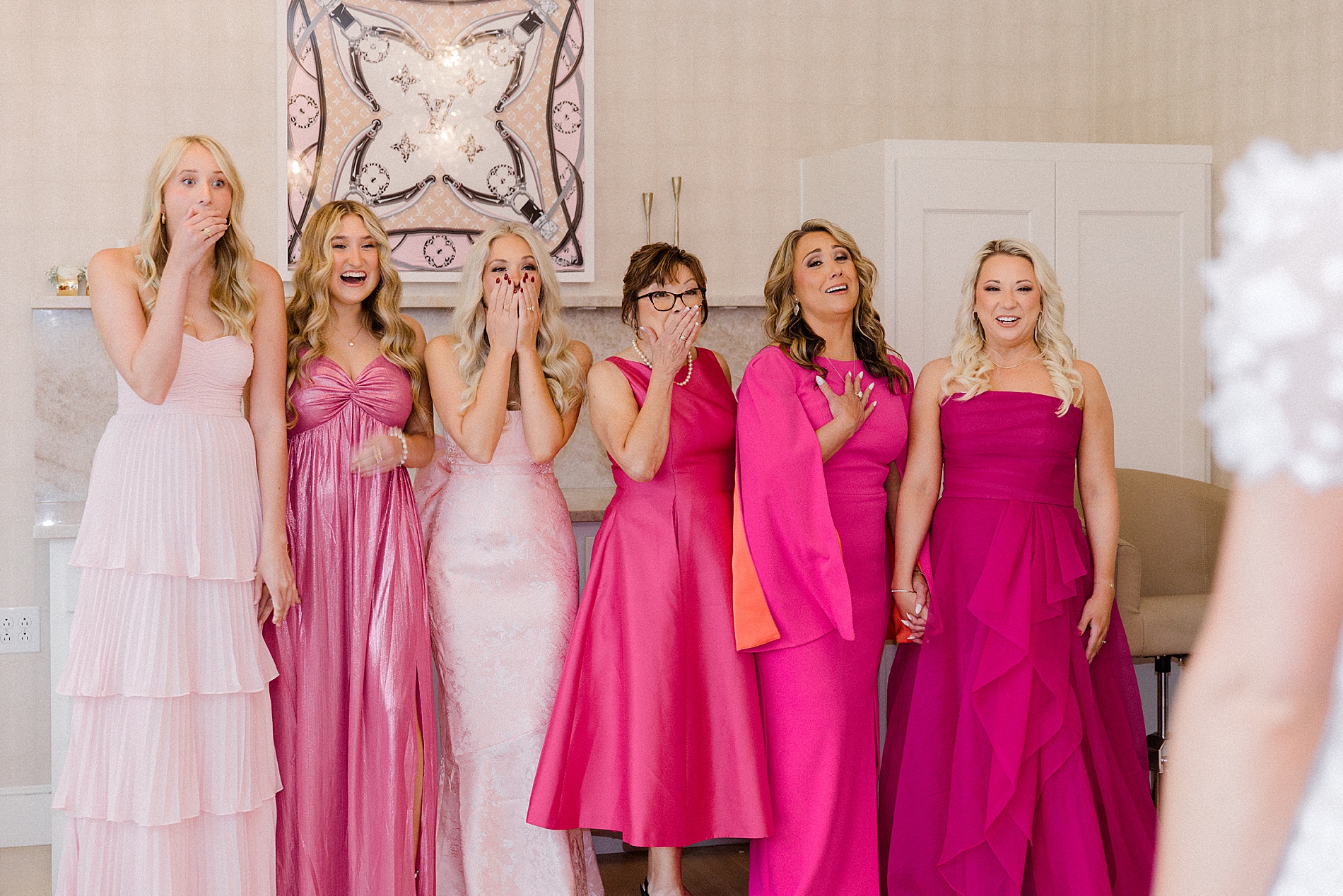 bridesmaids in dresses in various shades of pink react to seeing bride for the first time